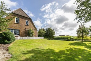 A brick house with a white picket fence, a well-maintained lawn, and a clear sky.