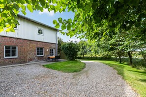 A building with a brick lower section and a white upper section, a gravel driveway, and a grassy area with trees.