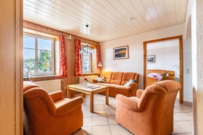 A room with a wooden ceiling, a sofa set, a table, and a window with curtains.