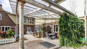 Un patio abrité avec un bâtiment en briques, une clôture blanche en bois et une table entourée de chaises.