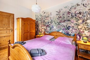 Un lit en bois avec une couverture violette, une armoire en bois et un papier peint à motifs floraux.