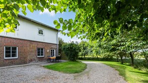 A building with a brick lower section and a white upper section, a gravel driveway, and a grassy area with trees. - Apartment 'Hooge' with Private Terrace, Shared Garden and Wi-Fi (Nordstrand)