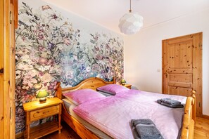 Une chambre à coucher avec un papier peint à motifs floraux, un lit en bois, une table de chevet avec une lampe et une porte en bois.