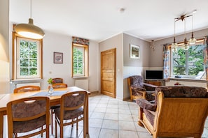 Un coin repas avec une table et des chaises en bois, un téléviseur et une fenêtre avec des rideaux.