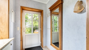 A hallway with a wooden door, a black doormat, a mirror, and a light fixture. - Apartment 'Hooge' with Private Terrace, Shared Garden and Wi-Fi (Nordstrand)