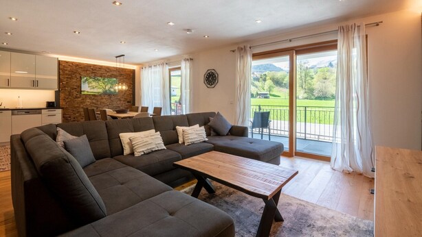 A modern living room with a sectional sofa, a wooden coffee table, and a dining area with a table and chairs. - Apartment in Tyrol near Kitzbühel (Jochberg in Tirol)