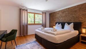 A bedroom with a bed, a desk, a chair, a window with curtains, and a brick wall. - Apartment in Tyrol near Kitzbühel (Jochberg in Tirol)