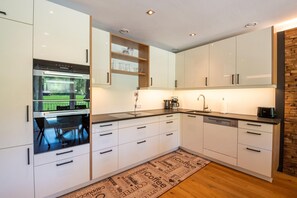 Una cocina moderna con armarios blancos, horno integrado y cafetera.