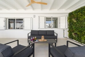 A modern outdoor seating area with a sofa and chairs, a table with drinks, and a green wall.