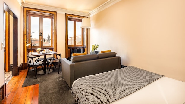 A compact hotel room with a bed, a sofa, a small dining table with chairs, and two windows offering a city view. - Beach studio nearby market in Oporto (Oporto)