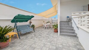 Eine Dachterrasse mit Schaukelstuhl, Tisch und Stühlen, Topfpflanzen und einer Treppe.