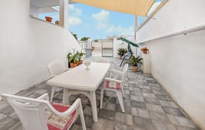 An outdoor patio with a white table and chairs, potted plants, and a view of buildings in the background.