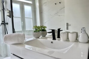 Un baño moderno con un lavamanos blanco, grifo negro y dos plantas en macetas.