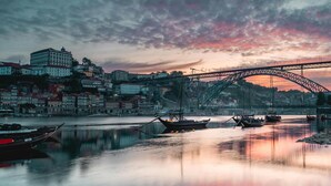 A bridge over a calm river with boats, a historic building, and a cityscape at dusk.