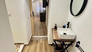 A narrow hallway with a wooden floor leading to a room with a white sink and a mirror on the wall. - Kensia house - historic center - central station (Palermo)