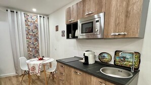 A compact kitchen with wooden cabinets, a stainless steel microwave, a sink, and a dining area with a table and chairs. - Kensia house - historic center - central station (Palermo)