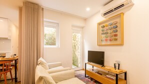 A modern living room with a sofa, a TV on a wooden stand, a dining area with a table and chairs, and a large window with curtains. - Charming 1-Bedroom Apartment in Oporto (Oporto)