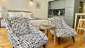 A modern hotel room with a bed, two patterned armchairs, a small round table, and a kitchenette. - Cozy Porto studio with balcony (Oporto)