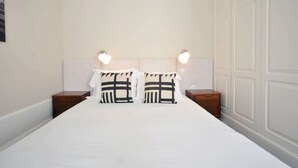 A neatly made bed with white bedding, two bedside tables with lamps, and a plain wall with paneling.