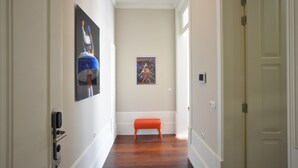 A hallway with a wooden floor, a bench, a door, and two posters on the wall.