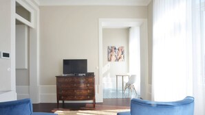 A room with a wooden dresser, a television, two blue chairs, a patterned rug, and a painting on the wall.