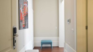 A hallway with a blue bench, a painting on the wall, and a door with a modern lock.