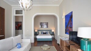 A modern hotel room with a large bed, a sofa, a TV, and a chandelier.