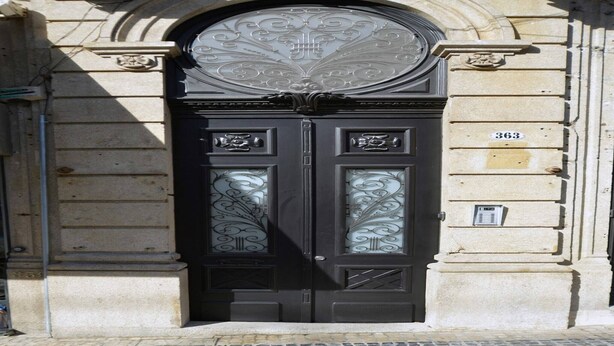 Eine schwarze Doppeltür mit aufwendigen Glasscheiben und einem Nummernschild am Gebäude.
