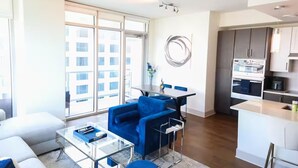 Un apartamento moderno con sala de estar que incluye una mesa de centro de vidrio, un sofá azul y una mesa de comedor.