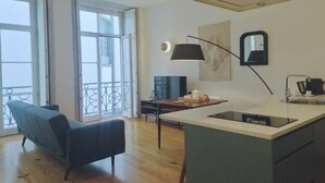 A modern kitchen with a central island, a dining area with a sofa, and large windows with a balcony.