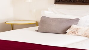 A neatly made bed with white and patterned pillows, a round gold table beside it, and a wall-mounted light fixture.