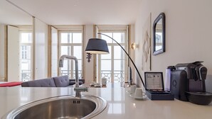 A modern kitchen with a stainless steel sink, a black lamp, a coffee machine, and a sofa.