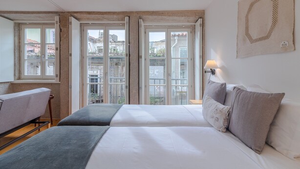 Un dormitorio con cama, mesita de noche, lámpara y vistas amplias por las ventanas.