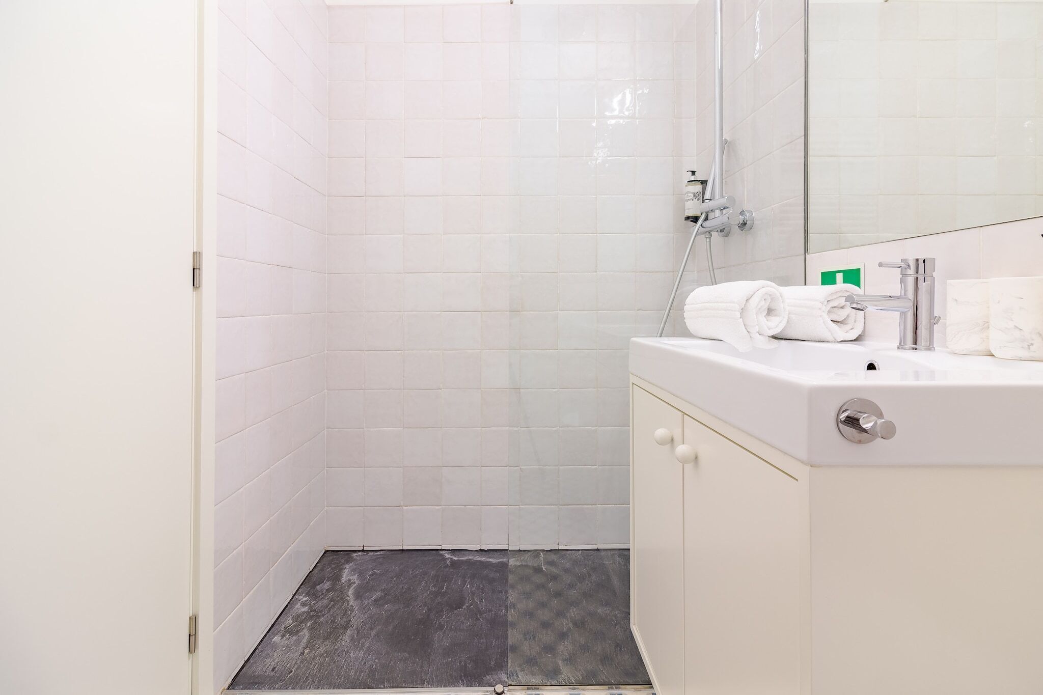A modern bathroom with white tiles, a shower, a sink with a mirror, and a toilet.
