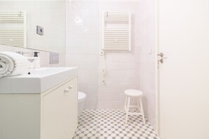 Ein Badezimmer mit einem weißen Waschbecken, einer Toilette und einer Dusche, inklusive weißem Handtuchhalter.