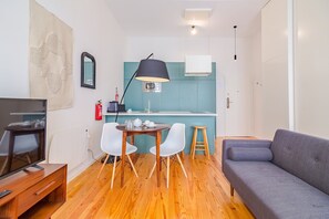 Ein kompakter Wohnraum mit Küchenzeile, einem Essbereich mit Tisch und Stühlen, einer Sitzecke und einem Fernseher.