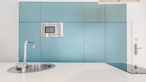 A modern kitchen with teal cabinetry, a stainless steel sink, and a built-in microwave. - Stylish Porto studio with city views (Oporto)