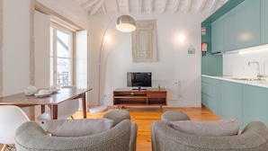 Una sala moderna con piso de madera, una mesa de comedor con sillas, un sofá, un televisor sobre un mueble de madera y una cocina con gabinetes color turquesa.