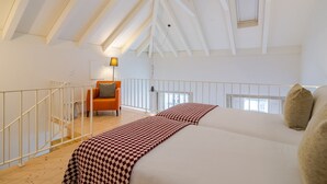 A high-ceilinged room with a sloped roof, a bed with a patterned bedspread, a chair, and a lamp. - Charming Porto apartment in prime location (Oporto)