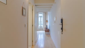 A hallway with a wooden floor, a door with a handle, a small table with a lamp, and a framed picture on the wall. - Charming Porto apartment in prime location (Oporto)