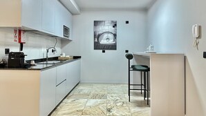 Eine moderne Küche mit weißen Schränken, einer schwarzen Arbeitsplatte und einem Marmorboden. Ein Barhocker und ein an der Wand befestigtes Telefon sind ebenfalls vorhanden.