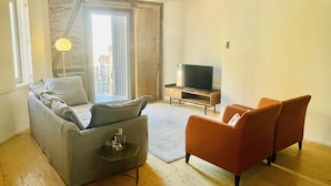 A living room with a grey sofa, orange armchairs, a TV, and a large window with curtains. - Trendy Studio in the Heart of Porto (Oporto)