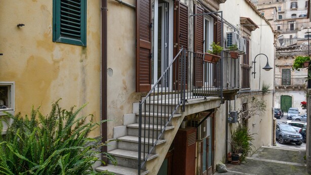 A narrow street with a building featuring a small balcony with a metal railing and potted plants. - Nice home in Modica with WiFi (Modica)
