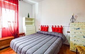 Une chambre à coucher avec un lit, une armoire, un miroir et une fenêtre avec des rideaux rouges.