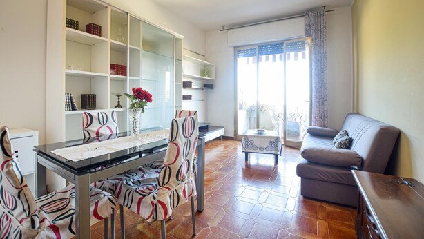 Un soggiorno moderno con zona pranzo, caratterizzato da una parete divisoria in vetro, un divano, un tavolo con sedie e una vista attraverso un'ampia finestra.