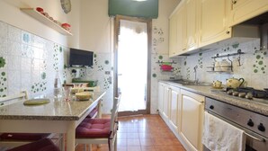 Una cucina con zona pranzo, una TV fissata sopra il bancone e una finestra con tenda.