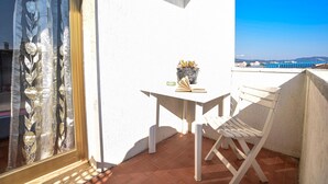 Un balcone con tavolo e sedia bianchi, una pianta in vaso e vista sul mare e sulle montagne.