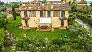 A two-story house with a tiled roof, a front garden with a lawn, and a small patio area with a table and chairs. - Cozy home in Castelfiorentino (Castelfiorentino)