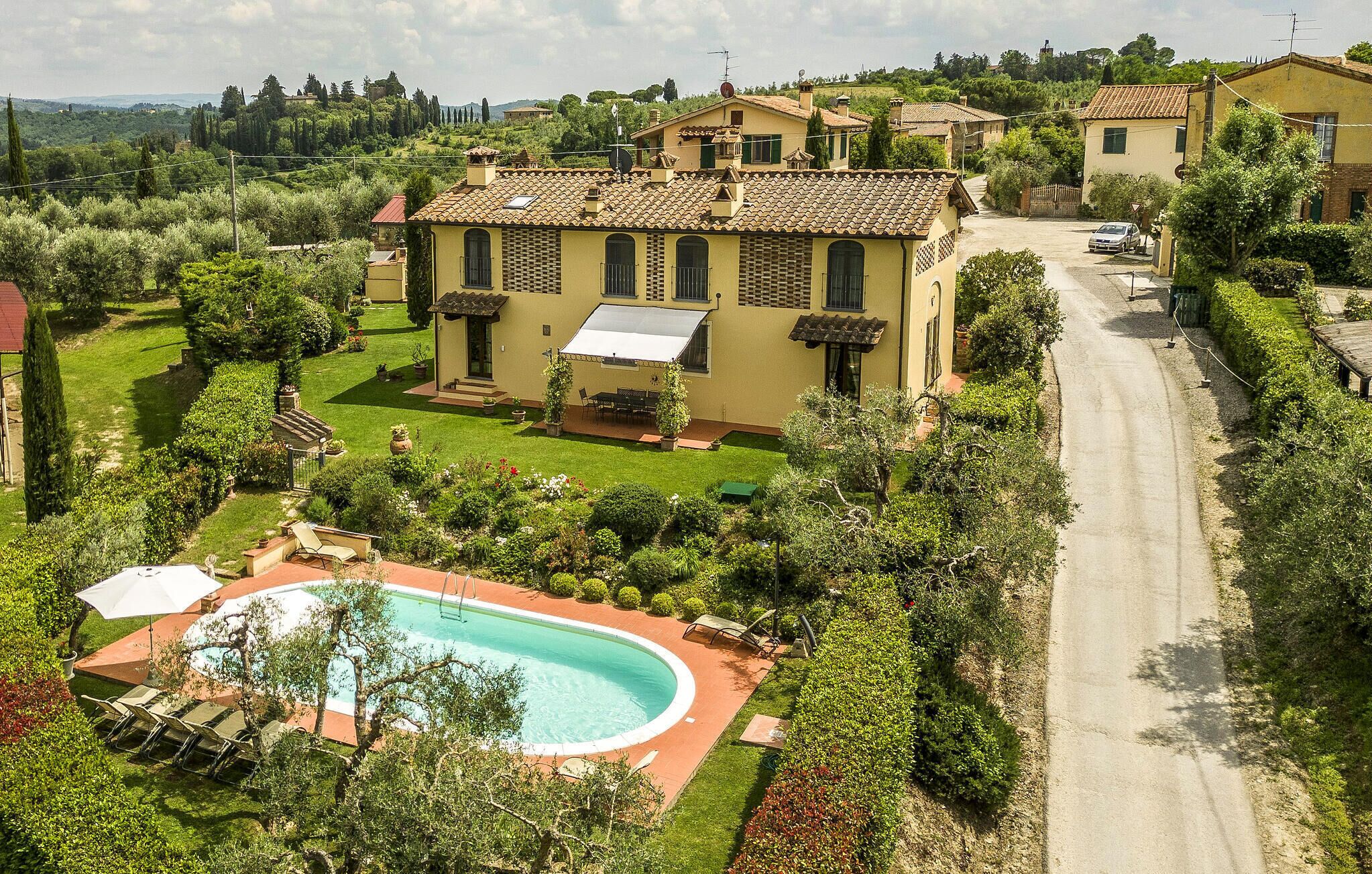 A villa with a swimming pool, surrounded by lush greenery and a clear road.