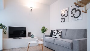 A modern living room with a grey sofa, a flat-screen TV, a small white table, and a potted plant. - Viale Lecco 105 in Como (Como)